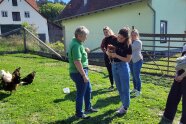 Mehrere Frauen stehen auf einer Wiese mit Hühnern. Eine Frau hält ein Huhn in den Händen.