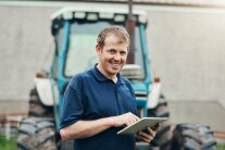 Landwirt mit einem Tablet-Computer vor einem Traktor