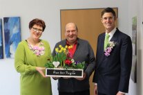 Schickes Paar mit Blumenschmuck überreicht Blumen an Herrn mit Glatze