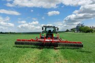 Traktor fährt über grünes Feld unte blauem Himmel