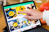 Finger zeigt auf Display eines Tablets, auf dem Bilder zubereiteter Lebensmittel zu sehen sind